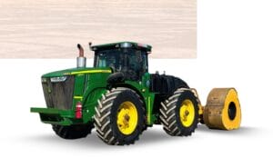 A green and yellow tractor with large tires is pulling a heavy, cylindrical roller on a bright, open area.