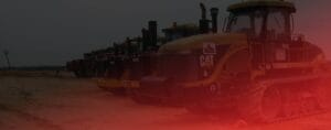 A row of construction vehicles, including Caterpillar machinery, parked in a line on a dirt surface. The image has a dark tint with a red gradient overlay on the right side.