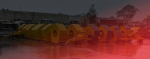 Yellow industrial machines lined up outdoors on a wet day with a building and trees in the background. A red tint partially covers the image, creating a warm hue.