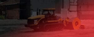 A construction vehicle with a caterpillar track and large blade pushes a rolled-up section of ground at the bustling site, highlighting the dynamic nature of industrial sectors. Overlaid with a red tint, the image exudes drama, while industrial buildings tower majestically in the background.