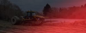 A large construction vehicle operates on a prepared dirt surface beside a lake, with leafless trees and dark skies in the background. With its focus on sustainable forestry, the image—with a red tint on the right—adds an artistic effect to highlight environmental harmony.