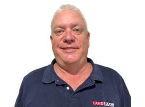A person with short white hair smiles at the camera, featuring a dark blue polo shirt adorned with a "LAND PAC" logo on the chest. The background is plain white, creating a simple yet striking composition. I'm sorry if this description is too brief for extracting specific SEO keywords.