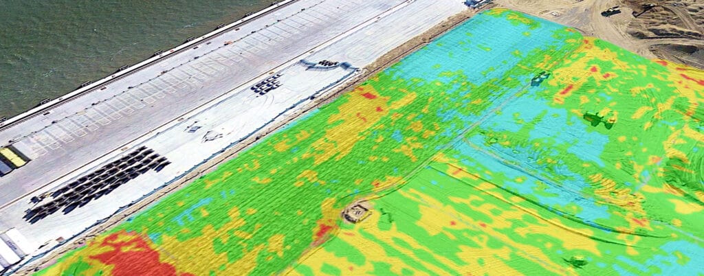 Aerial image showcasing a construction site blended with a colorful thermal map overlay. On the left, a concrete area with vehicles suggests active reporting of ground improvement services, while the right displays vibrant green, blue, yellow, and red terrain patterns.