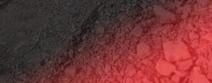 A rocky surface is partially illuminated by a red light, reminiscent of a demolition site. The uneven ground, akin to one after concrete breaking, is covered with various sizes of stones and pebbles, creating a rough texture. Shadows and light variations add depth to the scene.