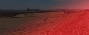 A vast, barren landscape with a single construction vehicle in the center, surrounded by mounds of coal discard. The scene is bathed in a faint red hue under a clear sky.
