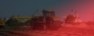 A large bulldozer moves across a construction site on Kooragang Island, with piles of sand and heavy machinery in the background. The image, overlaid with a red tint, highlights the proximity to the bustling coal export terminal.