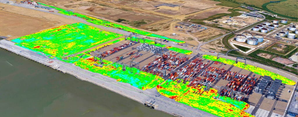 Aerial view of the London Gateway, showcasing a bustling port with numerous shipping containers neatly organized in rows. Adjacent areas display bright green and yellow overlays indicating varying levels of logistics activity or vegetation. Industrial buildings and tanks loom in the background.