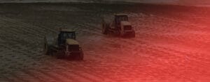 Two tractors plowing a muddy field under poor weather conditions, with a red glare partially covering the scene. Set in a rural landscape, this image echoes the industrious spirit of Tuas Terminal’s Phase 1, highlighting diligent agricultural activity amidst challenging elements.
