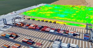 An aerial view of a bustling port reveals applications of logistics with colorful shipping containers arranged in rows. Adjacent is a vast open area with a digitally overlaid green and yellow thermal map, showcasing efficient space management. Cranes and tracks are visible near the containers.