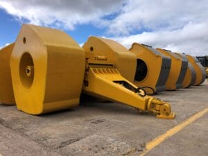 A row of large, yellow, heavy machinery components with circular ends stands aligned on a concrete surface under a cloudy sky, captured in vivid detail thanks to the HEIC image format.