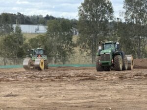 Two tractors with rollers compact uncontrolled fill on a construction site surrounded by trees.