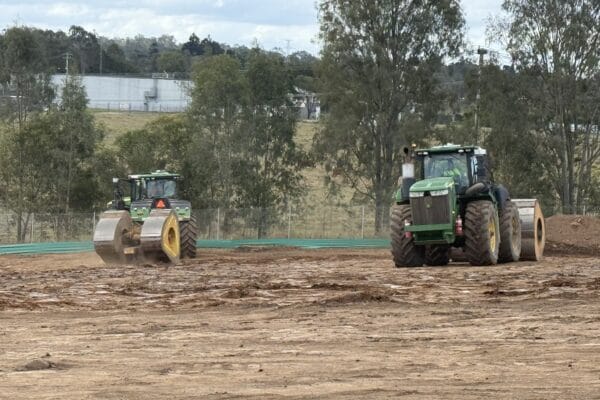 Two tractors with rollers compact uncontrolled fill on a construction site surrounded by trees.
