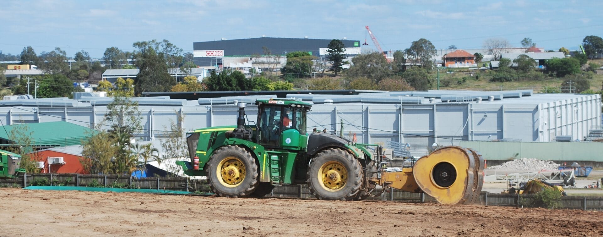 A green tractor flattens uncontrolled fill with a large roller at a construction site.