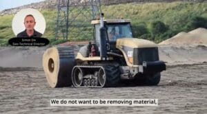 A Caterpillar tractor on sand, with an inset of Simon Dix speaking and subtitles displayed.