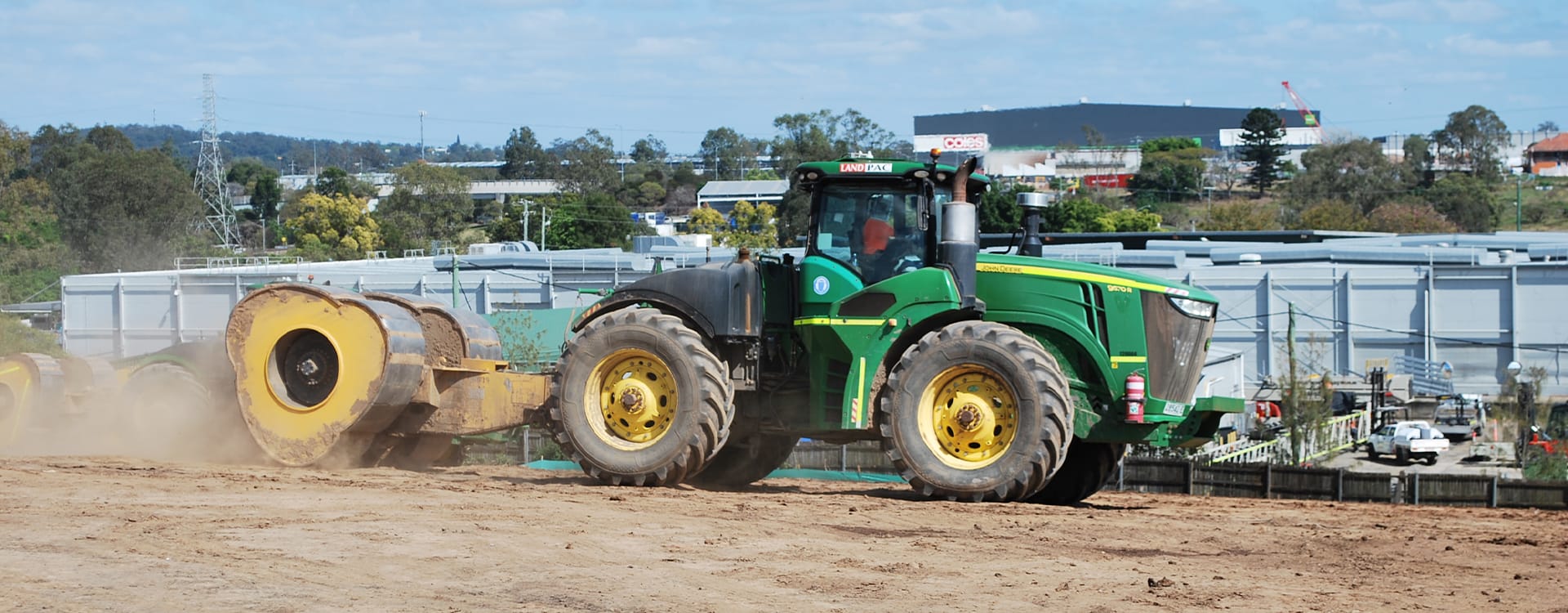 A green John Deere tractor pulling a yellow soil compactor at a sand to clay interface site.