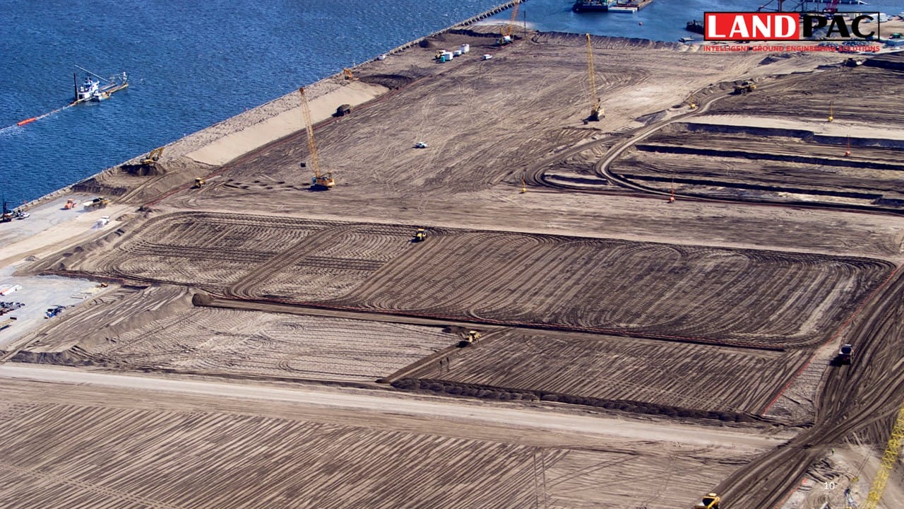 Aerial view of large-scale land grading near water, with equipment and cranes at work.