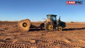 A tractor with large roller wheels works on a flat, dry construction site under a clear sky.